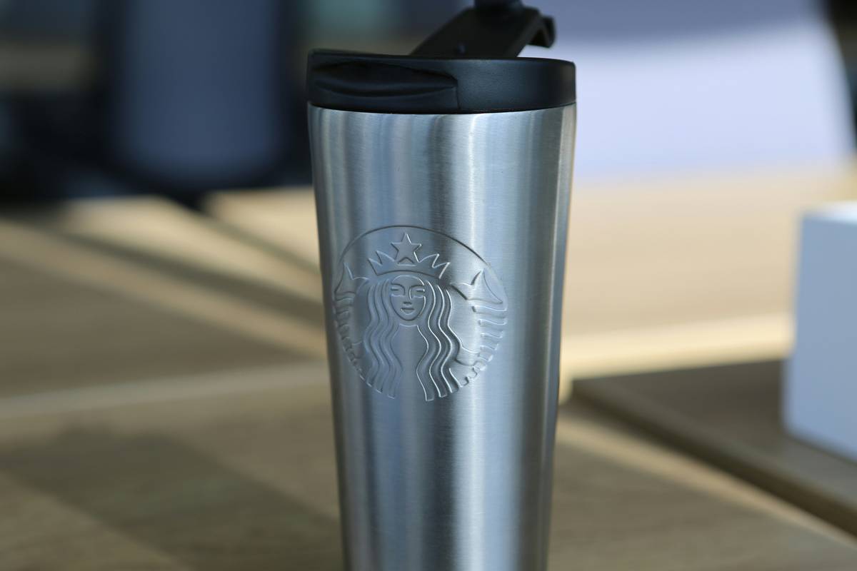 A hand holding a drinkware stainless steel coffee mug made with double-wall insulation on a wooden kitchen counter