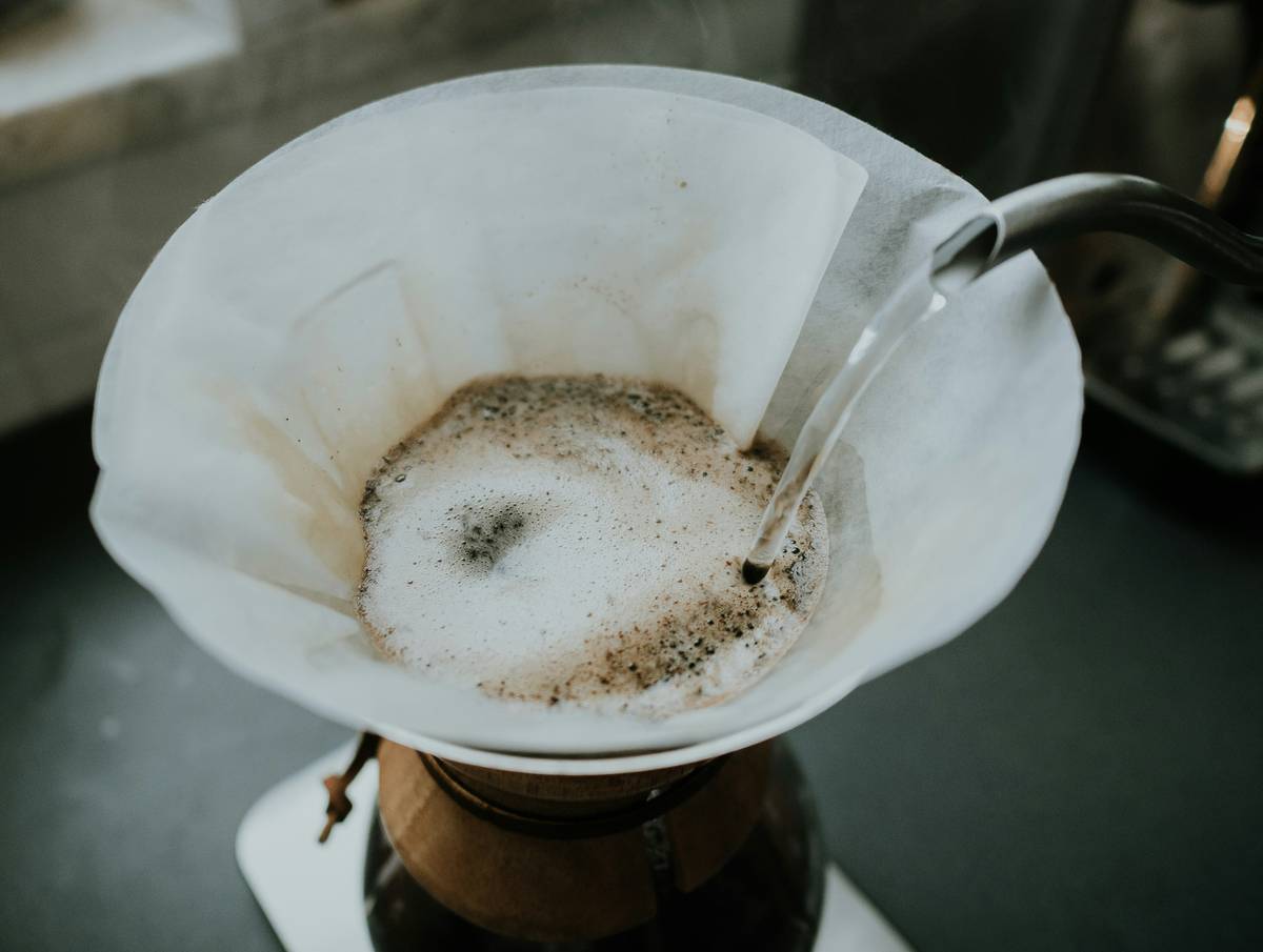 Stainless steel coffee mug beside eco friendly coffee maker on wooden countertop